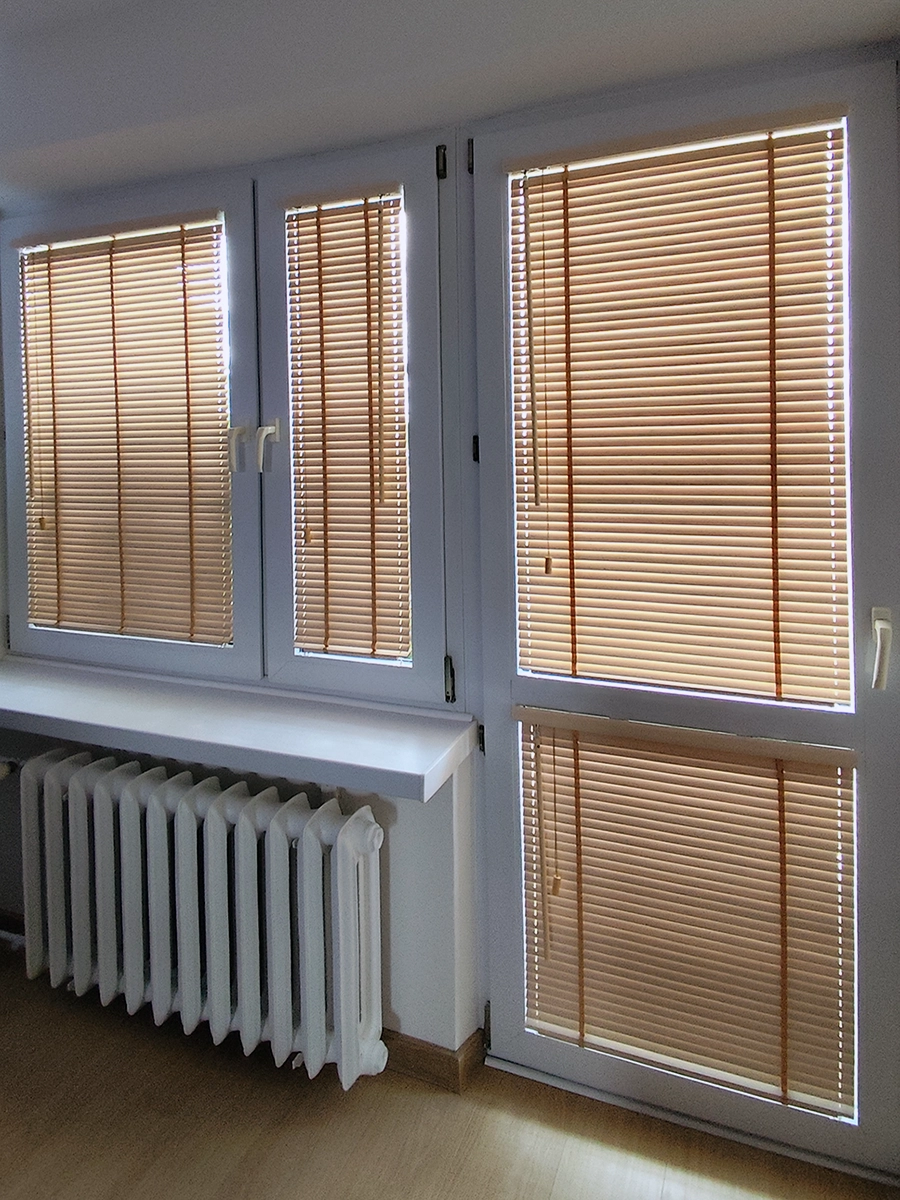 Jasne żaluzje drewniane 25 mm na oknie balkonowym i oknie w salonie