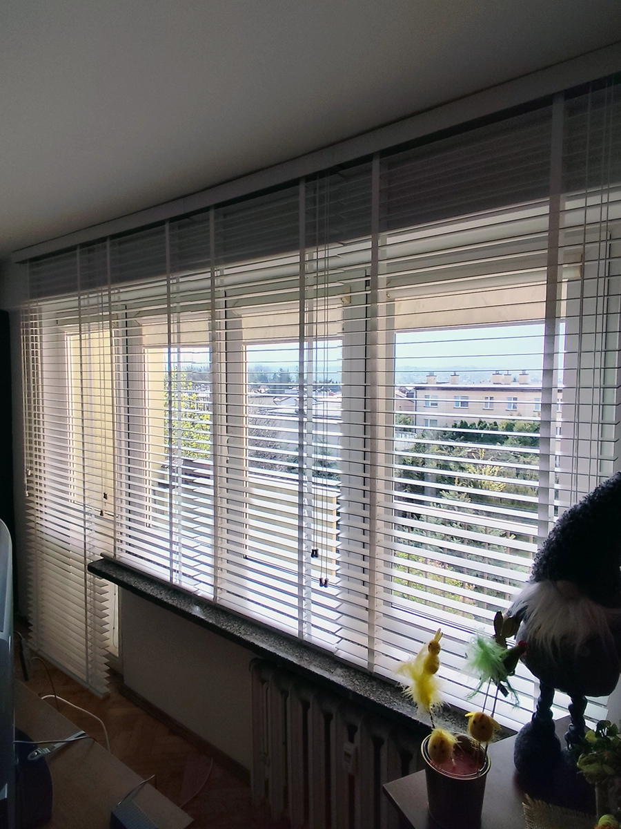 Białe żaluzje drewniane 50 mm na taśmach w dużym oknie