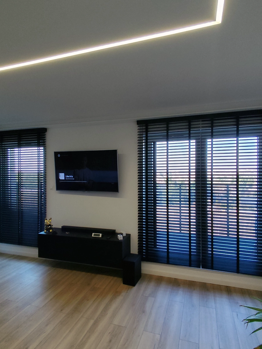 Czarne żaluzje drewniane 50 mm w nowoczesnym salonie na dużych oknach