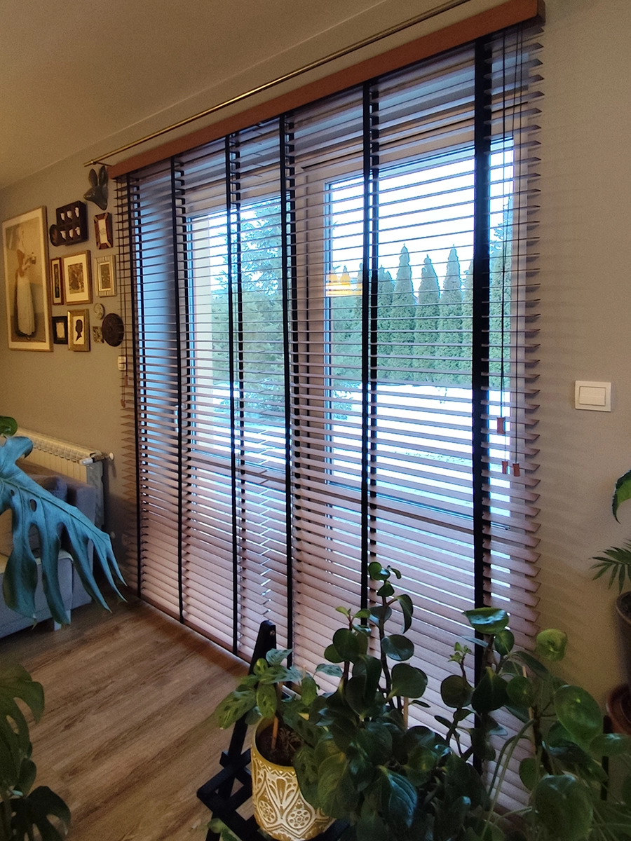 Jasne żaluzje drewniane 50 mm na dużym oknie w salonie