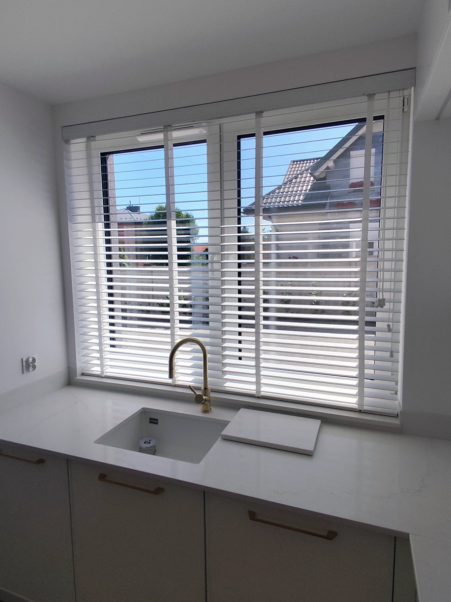 Białe żaluzje drewniane 50 mm w nowoczesnej kuchni przy dużym oknie